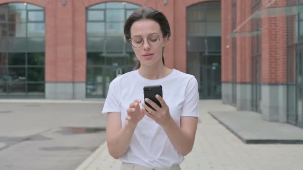 Beautiful Young Woman Browsing Internet on Smartphone while Walking on Street