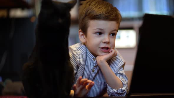 Funny Child with Kitten Using a Laptop at Home.