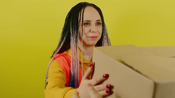 Young Woman in Vest with Cardboard Box on Yellow Background in Studio