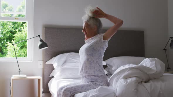 Senior caucasian woman stretching her arms while sitting on the bed at home