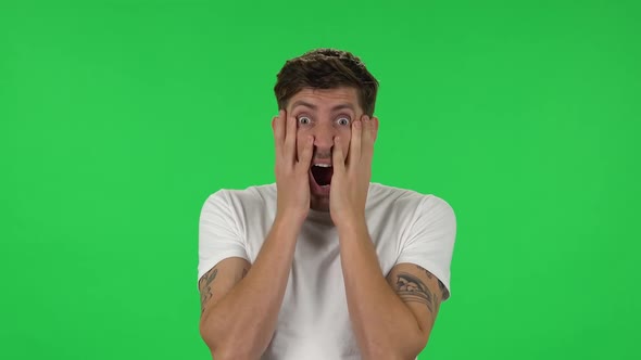 Portrait of Confident Guy Horror Looking and Covers His Face with His Hands. Green Screen