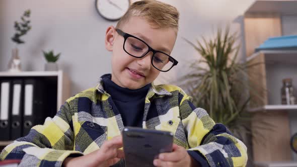 Smiling Handsome Teen Boy in Glasses which Holding Phone in His Hands and Watching on Screen