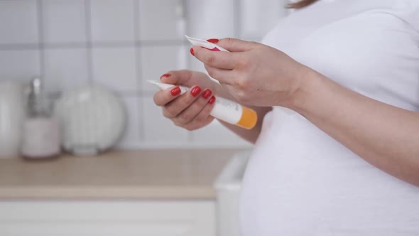 Pregnant Woman Hands with Smartphone Reading Label on a Bottle