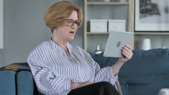 Online Video Chat on Tablet By Old Senior Woman Sitting on Couch