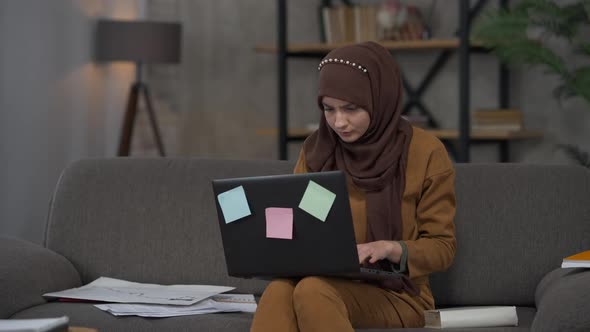 Young Exhausted Woman in Hijab Closing Laptop Sighing and Leaning Back on Couch