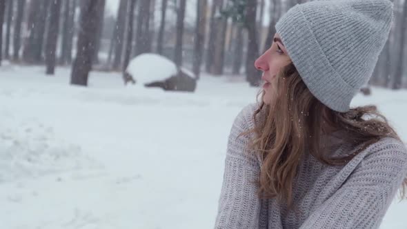 Cute Caucasian Girl in a White Sweater and Hat in a Snowy Forest Park Drinking Hot Tea or Chocolate