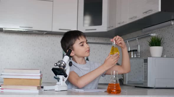 The Boy Learns Chemistry Using a Microscope and Flasks with Liquid and Makes Notes in a Notebook