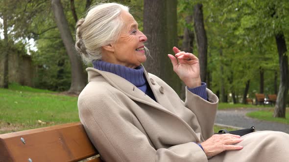 An Elderly Woman Sits on a Bench in a Park and Celebrates