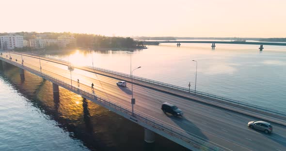 Tracking aerial shot of a bridge in Helsinki during sunset. Cars and cyclists are visible on the bri