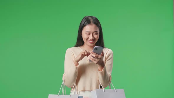 Asian Woman With Shopping Bags Enjoy Using Mobile Phone Shopping Online At Green Screen