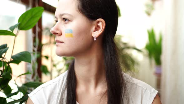 Portrait of Young RussianUkrainian Girl with the Flag of Ukraine and Russia on Her Face