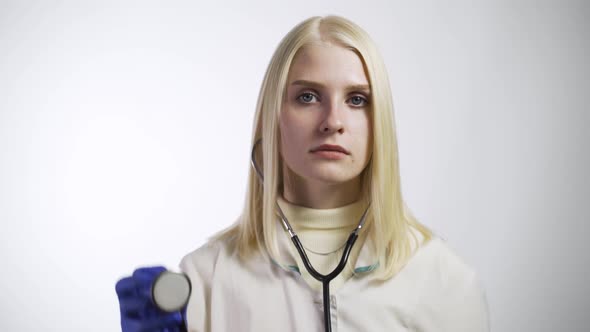 Young Female Doctor Seriously Looks Into the Camera and Raises Up a Stethoscope