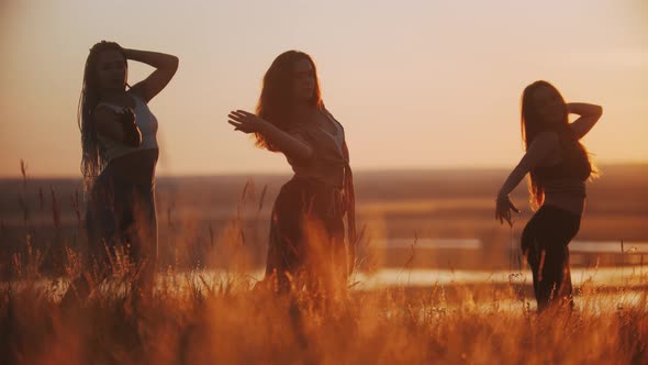 Three Young Women Doing Aerobic Dance and Slow Movements with Their Hands on Sunset