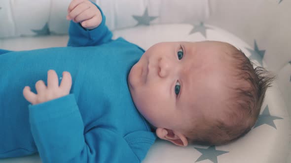 Upset Little Boy Lies in Sleeping Cocoon with Stars in Cot