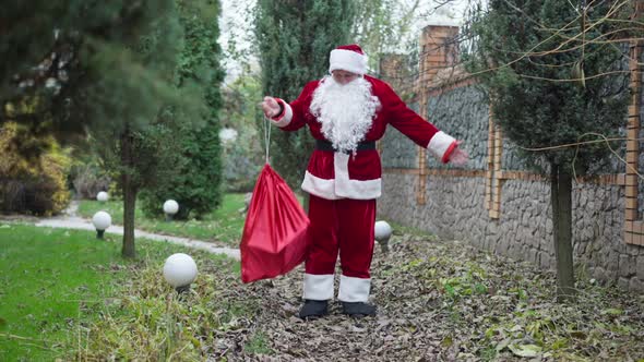 Wide Shot Santa with Gifts Bag Standing on Backyard with Green Trees