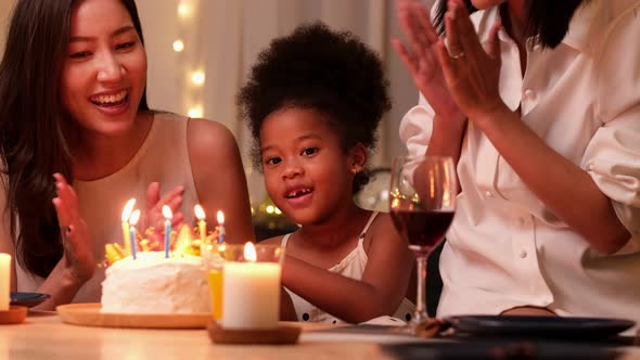 Happy little girl celebrating her birthday with Lgbt family blowing out the candles