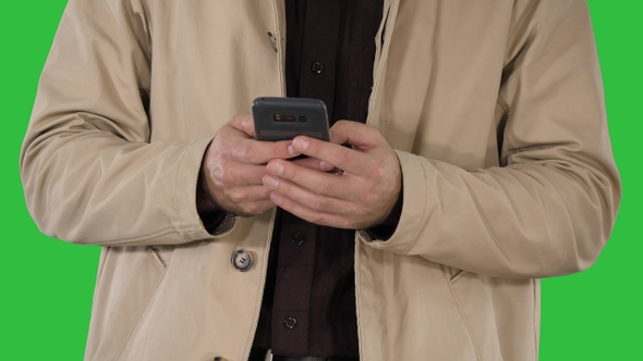 Man in trench coat using mobile smart phone on a Green