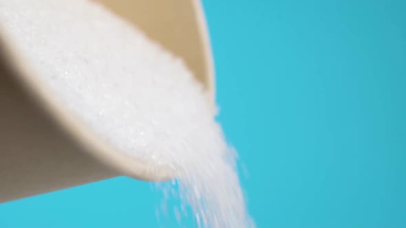 Sugar is poured from a full paper cup. On a blue background