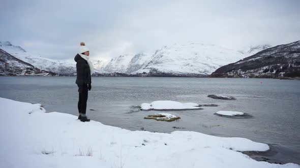 Young asian woman walking on pond shore against highland in winter