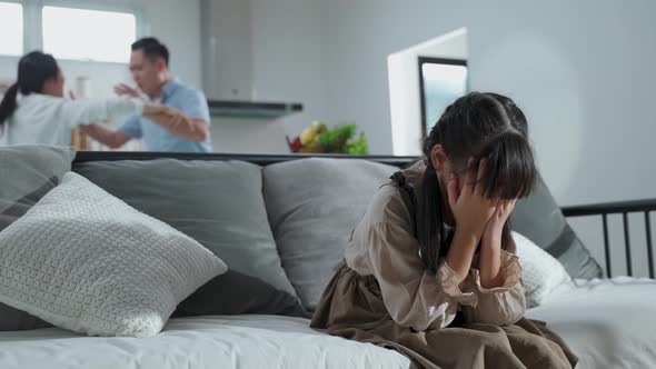 Asian girl kid sitting and crying on bed while parents having fighting or quarrel conflict at home.