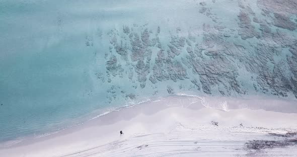 One man walking at the beach in soft morning light with blue transparent water on his side. People