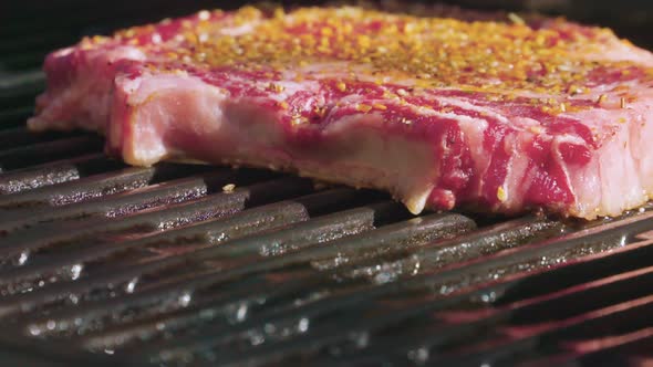 Delicious, seasoned ribeye steaks cooking on a grill.