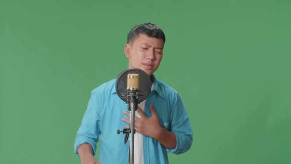 Young Asian Boy Singing Into Microphone In Green Screen Studio
