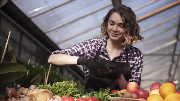 Low Angle View of a Beautiful Smiling Woman Farmer in Black Gloves Arranging Organic Food in Farm