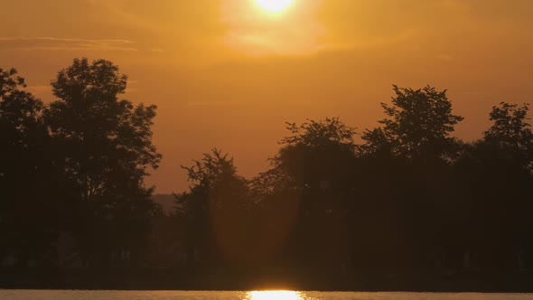 Lakeside Landscape with Dark Silhouette of Park Trees Reflected in Lake Water and Distant Walking