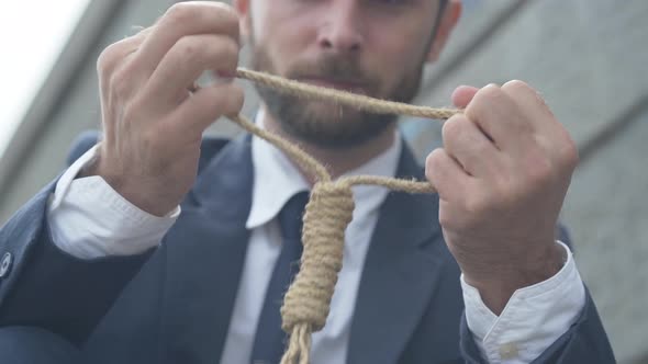 Close-up of Male Caucasian Hands Holding Rope with Blurred Young Man Thinking at the Background