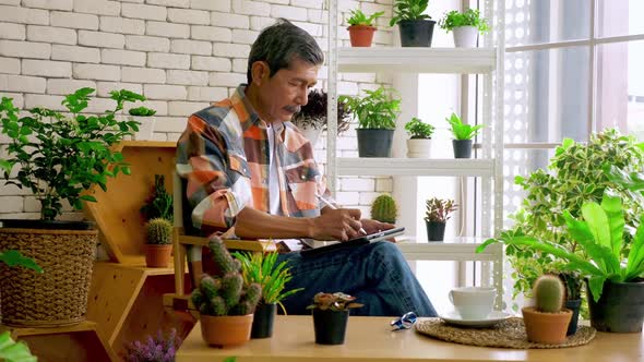 An old man sitting in a living room decorated with flower pots.