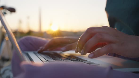 Lady Freelancer Types Information on Laptop at Back Sunset