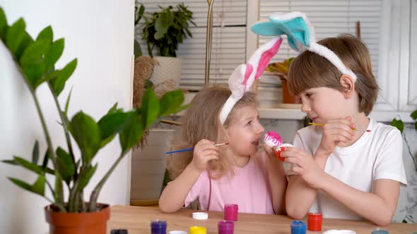 a Little Girl and a Boy with the Ears of Easter Hares Paint Eggs for the Holiday with Brushes
