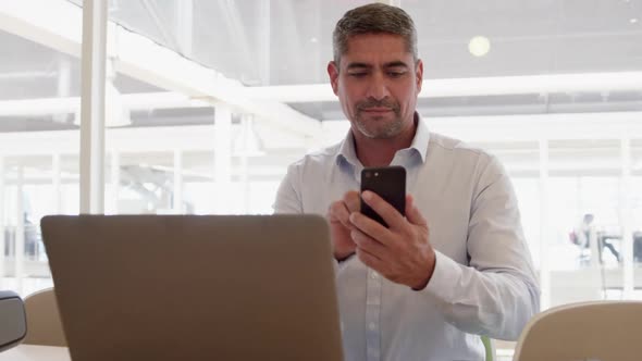 Businessman using mobile phone while working on laptop in modern offi 4k