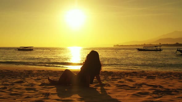 Silhouette of girl meditating on exotic beach at magical sunset with yellow sky reflecting over tran