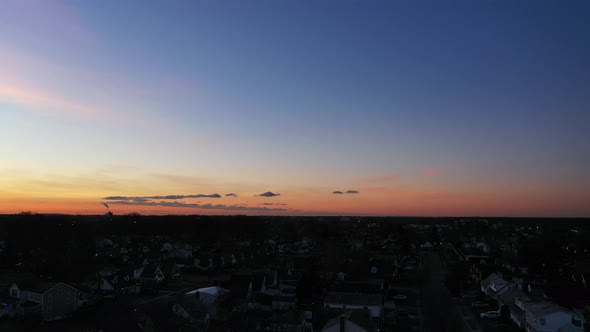 An aerial shot over a suburban neighborhood at sunrise. The camera dolly in towards the horizon whil