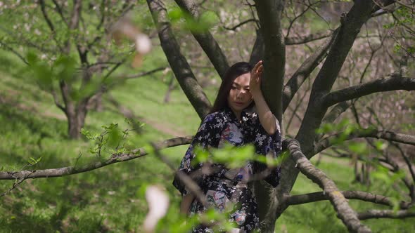 Slim Beautiful Asian Woman Standing at Tree in Spring Park Looking Away