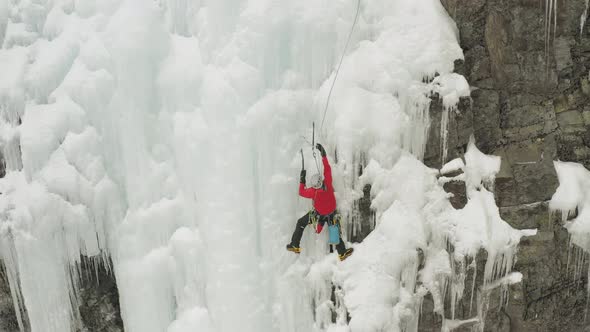 Single climber on frozen ice cascade preparing safety line 4K