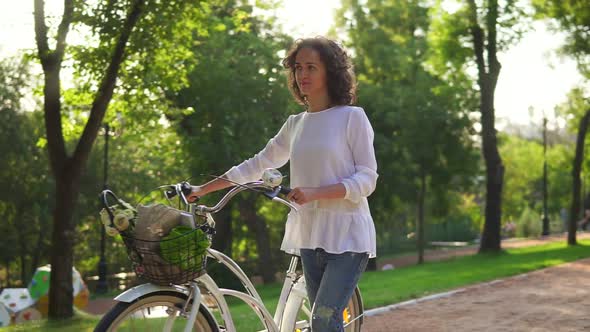 Attractive Woman in a White Shirt and Blue Jeans Walking on the Alley in the City Park Holding Her