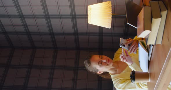 Business Woman in a Yellow Sweater is Pensively Writing Notes in Front of a Laptop