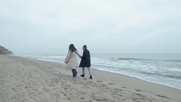 Happy Couple Walking on the Wild Beach on Cloudy Sunrise or Sunset