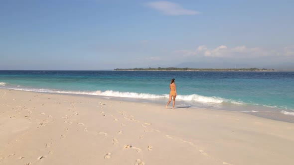 Young Woman with bikini running towards ocean beach and raising up her arms.Aerial flyover Gili Meno