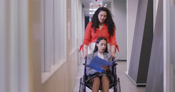 Happy biracial businesswoman with disabled colleague in wheelchair working together in modern office