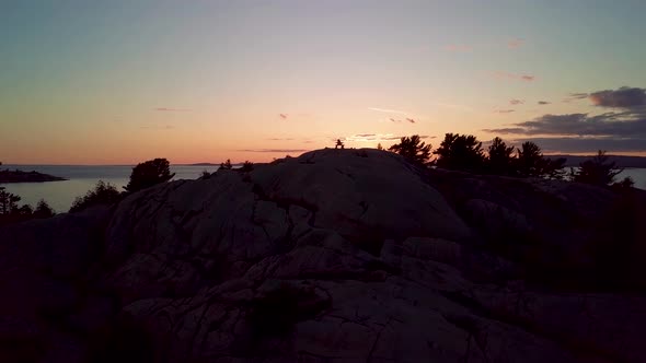 Inukshuk on Top of Rocky Pine Tree Island at Sunset, Drone Aerial Wide Orbit Pan. Reveal of Blue Lak