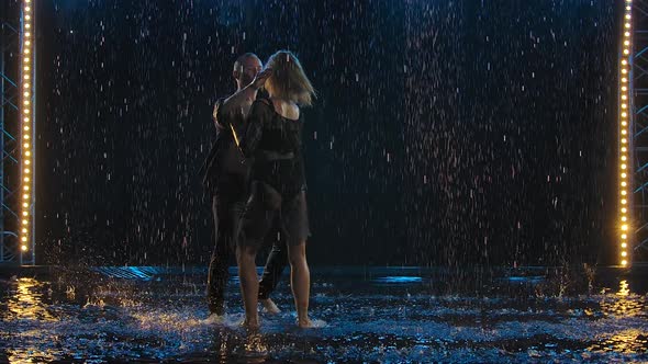 Active Happy Adults Dancing Salsa Together in a Dark Studio in the Rain. A Couple in Black Are