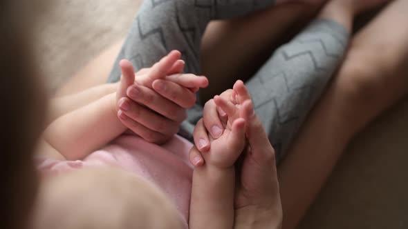 Mom's hands caress the hands of her little daughter, top view