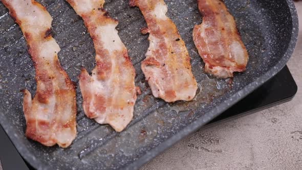 Cooking Pieces of Flavorful Sliced Organic Bacon Fried in Grill Pan