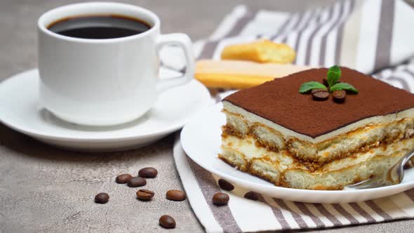 Portion of Traditional Italian Tiramisu dessert and cup of coffee on grey concrete background