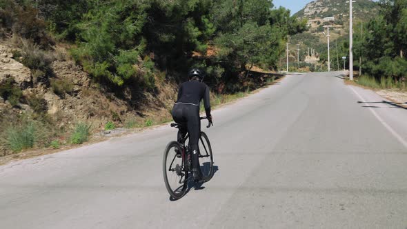 Female cyclist is riding bicycle on empty forest road