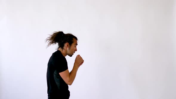 Focused Ethnic Man with Long Hair and Goatee Shadowboxing in Front of White Studio Backdrop